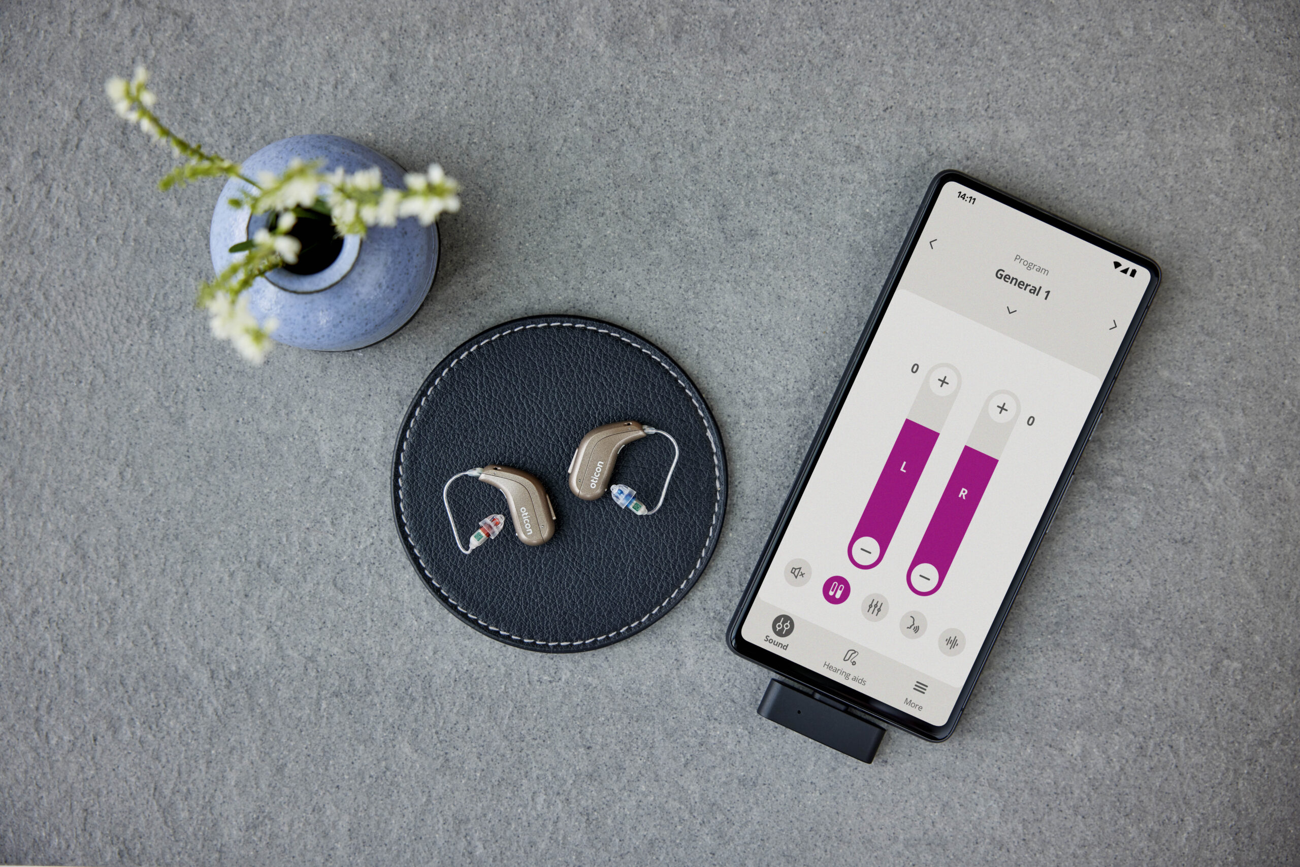 Zwei Oticon Intent Hörgeräte neben einem Smartphone mit geöffneter Hörgeräte-App