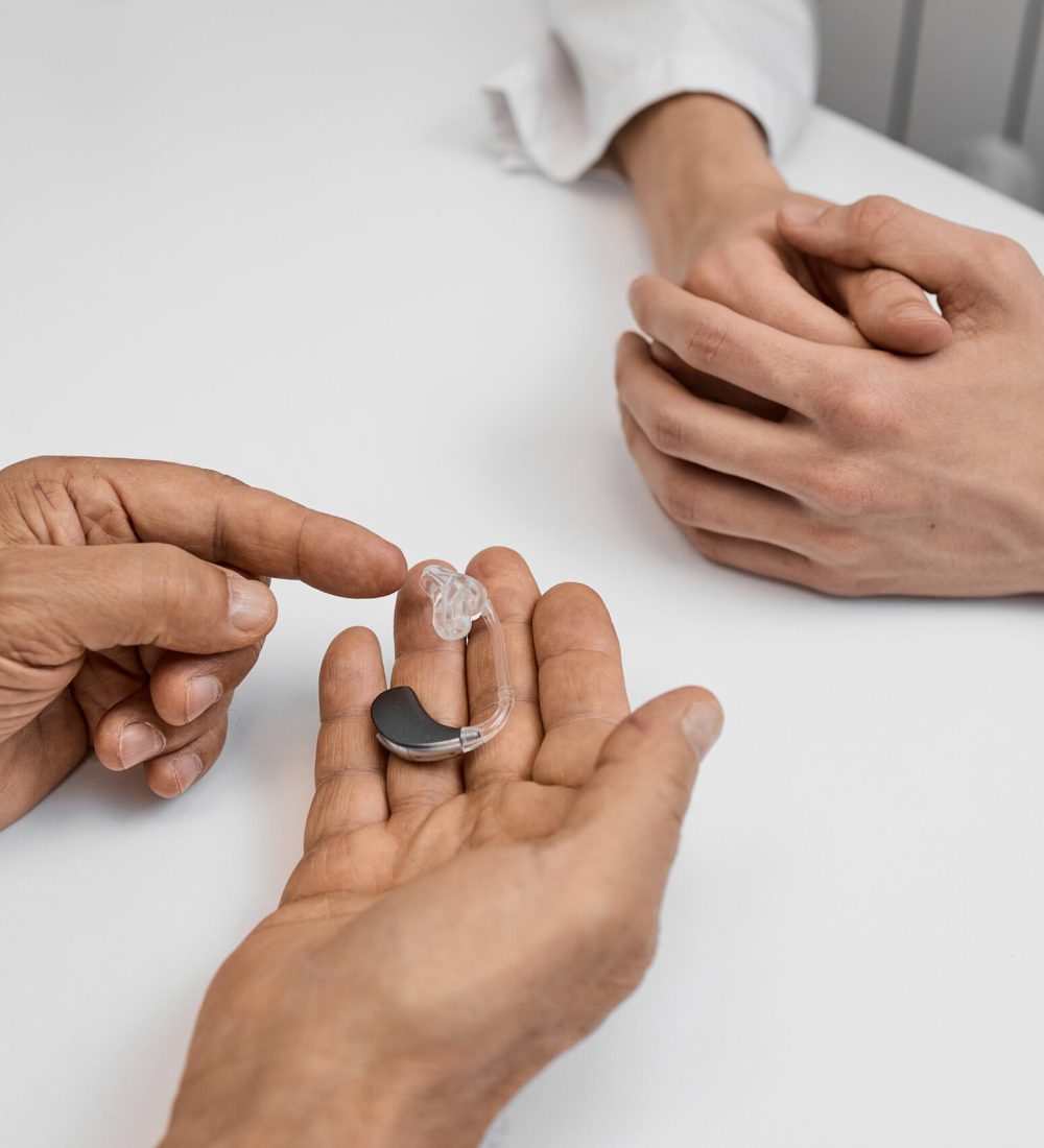 During a consultation, a patient examines a behind-the-ear hearing aid with a doctor assisting in the process